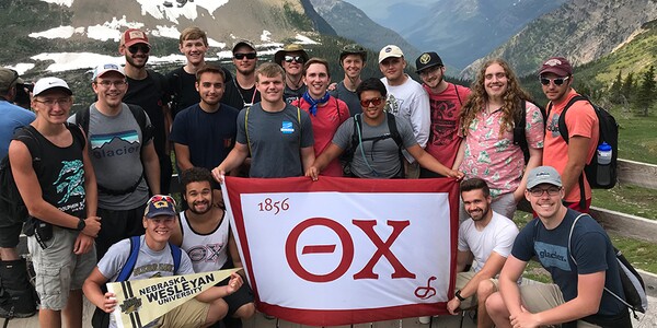 Several Theta Chi members holding banner in front of a glacier.