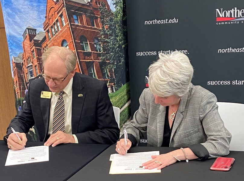 NWU President Darrin Good and Northeast Community College President Leah Barrett sign a document in front of them.