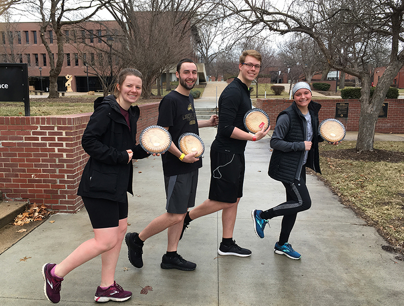 Four students holding pies pretending to run