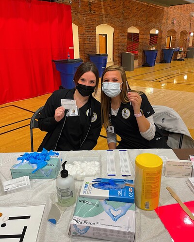 Two nursing students sitting in front of a table with vaccination supplies.