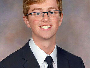 Kyle Goodban wearing glasses and a tie smiles.