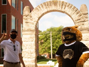Masked President Good and Prairie Wolf in front of NWU Arch