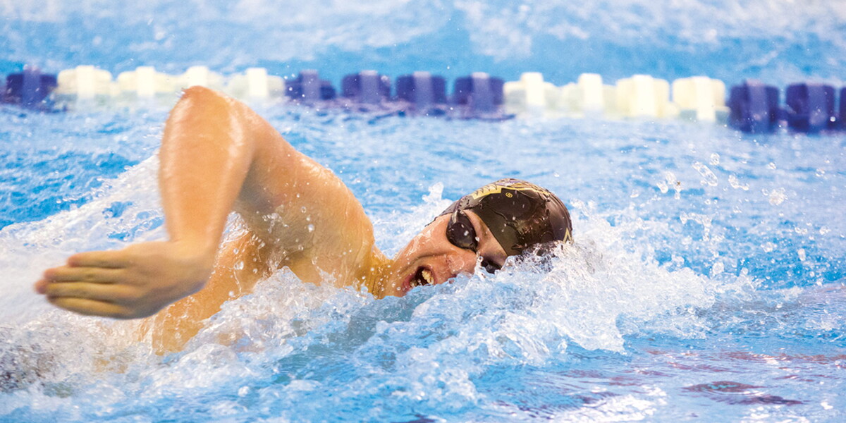 Male swimmer with goggles and skin cap swimming in lane of a pool.