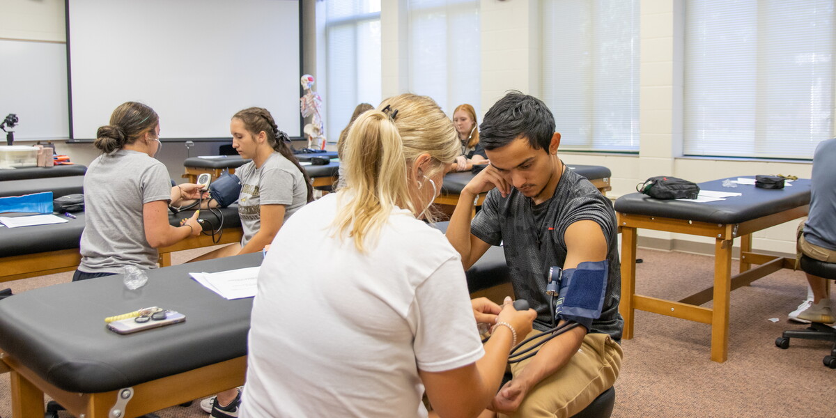 Students in a classroom paired up taking blood pressure.