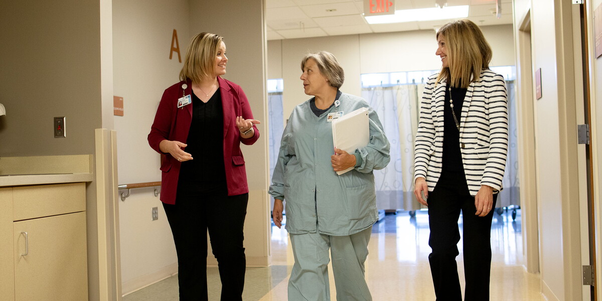 Three women walk down a hospital hallway.