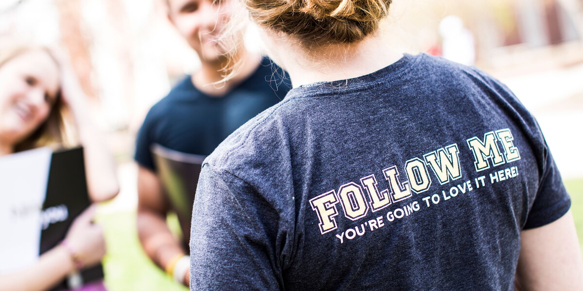 Woman with her back to the camera in a shirt that says, 'Follow Me'.