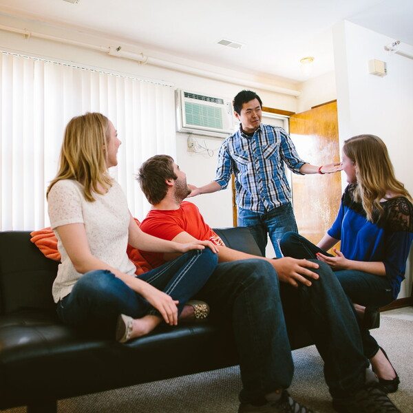 Young man walks into the living room where three friends are sitting on a couch.