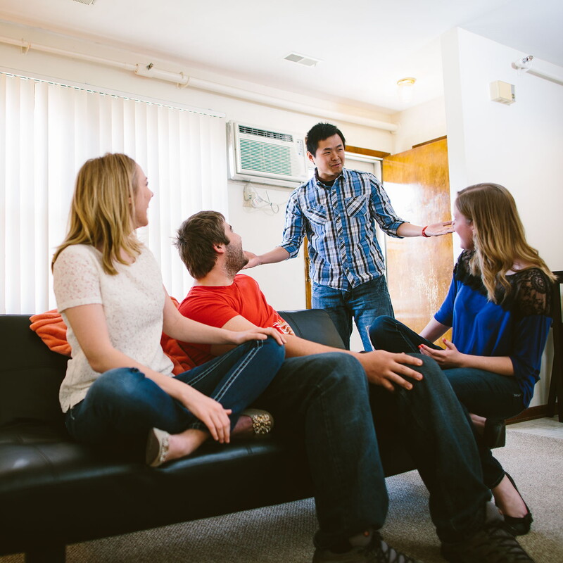 Young man walks into the living room where three friends are sitting on a couch.
