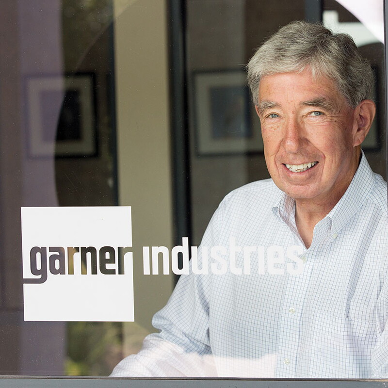 Head shot of Philip Mullin behind a glass door with a logo that says, Garner Industries.