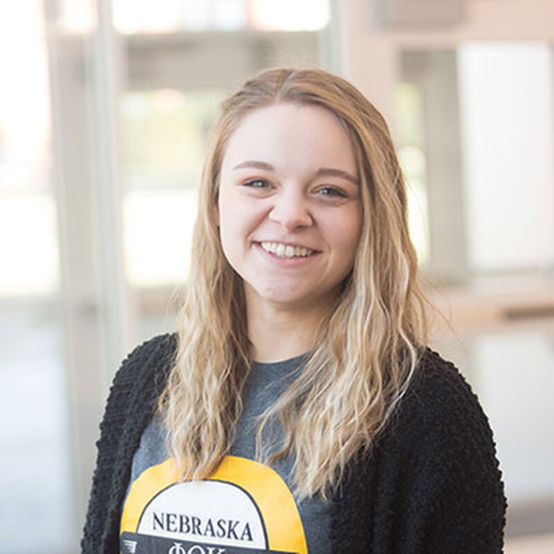 Young woman smiling standing in front of glass doors.