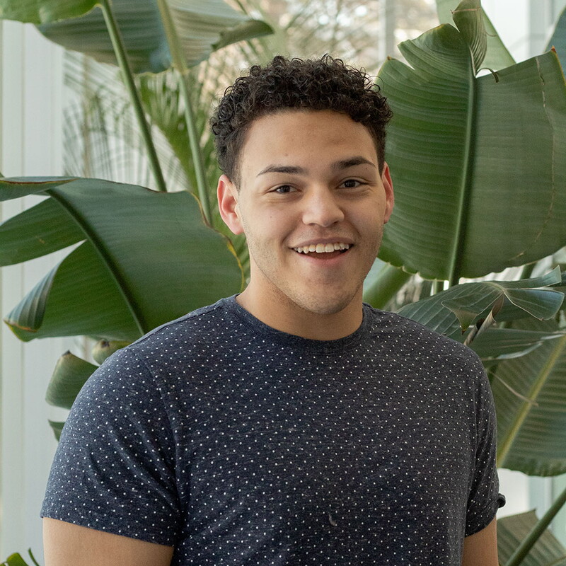 Young man standing in front of a plant smiling.