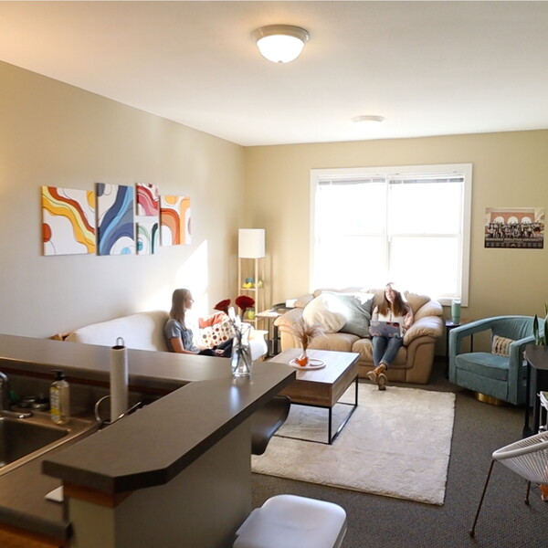 View of a townhouse apartment from the kitchen into the living room. Two young women sitting in the living room.