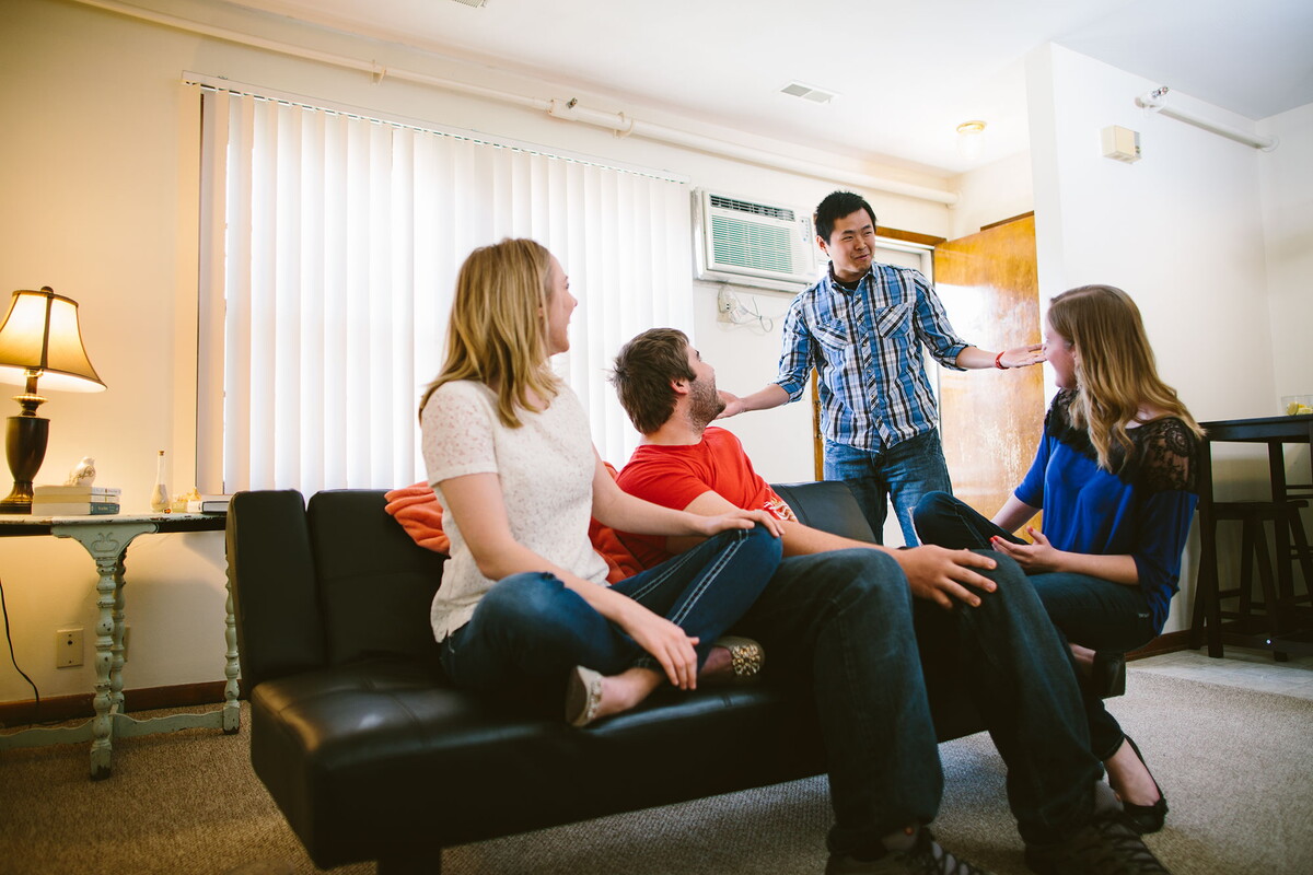 Man enters apartment into the living room with three people turned to talk to him.