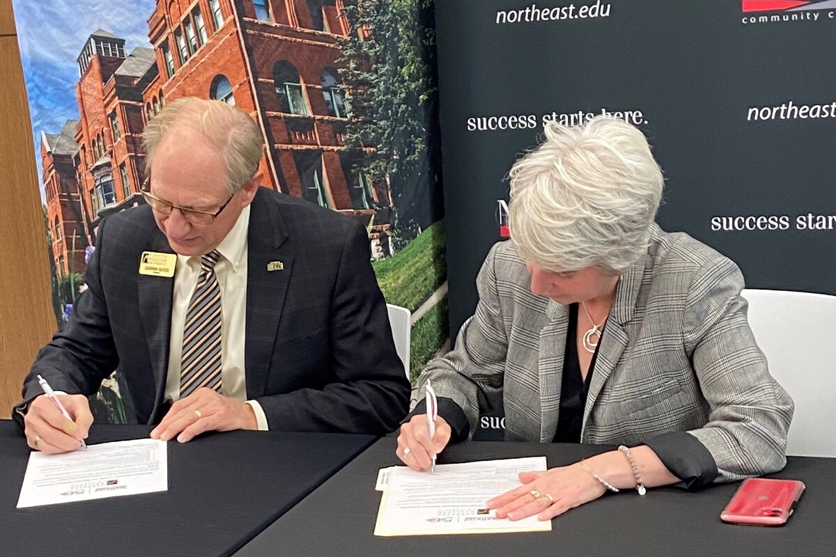 NWU President Darrin Good and Northeast Community College President Leah Barrett sign a document in front of them.