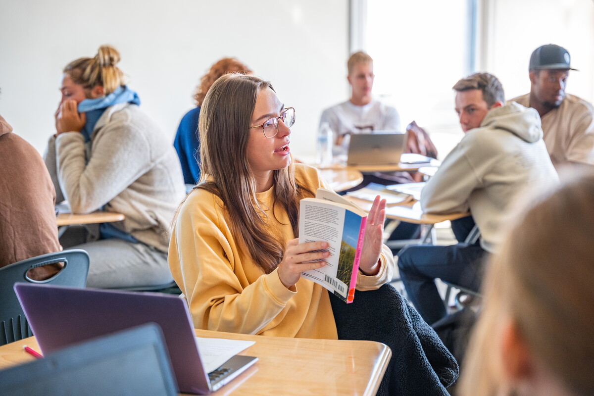 A student in a classroom talking to classmates.