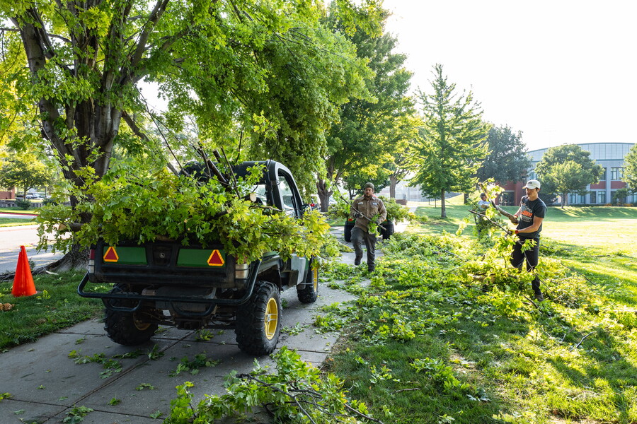 Outside by some trees, maintenance staff cleaning up down tree limbs.