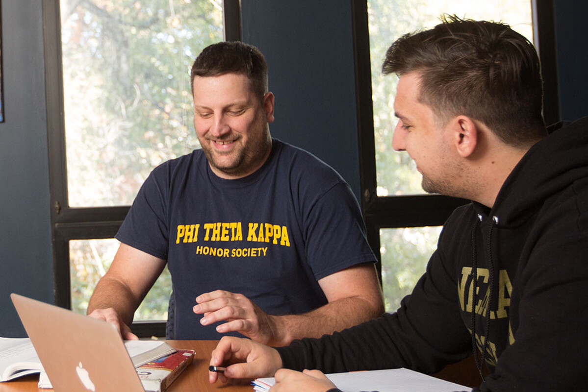 Two male students at a conference table. One students sweatshirt reads Phi Theta Kappa Honors Society.