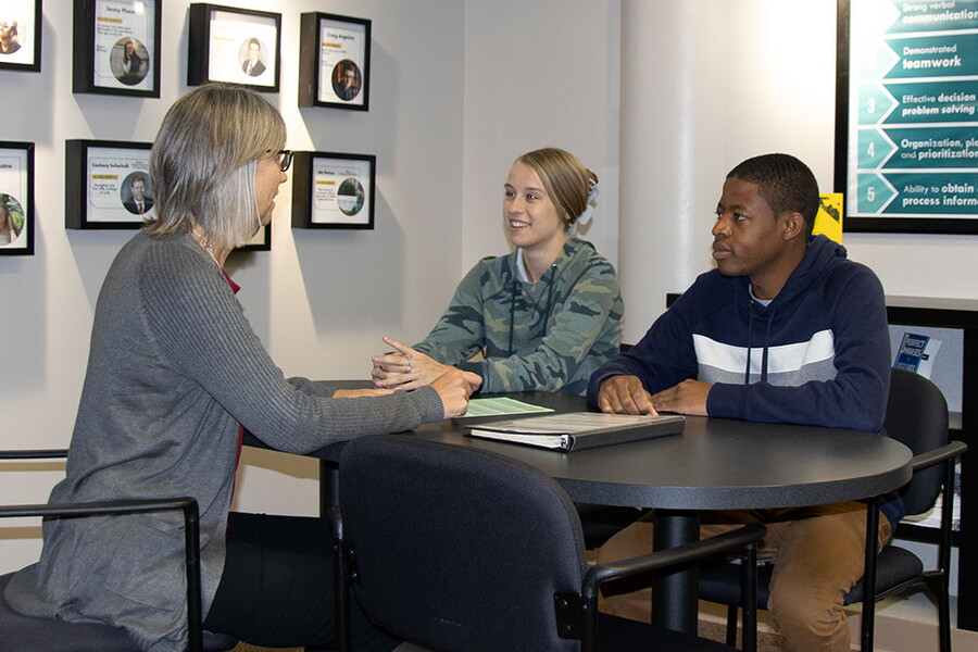 NWU administrator sits with two students at a table in a conference room.