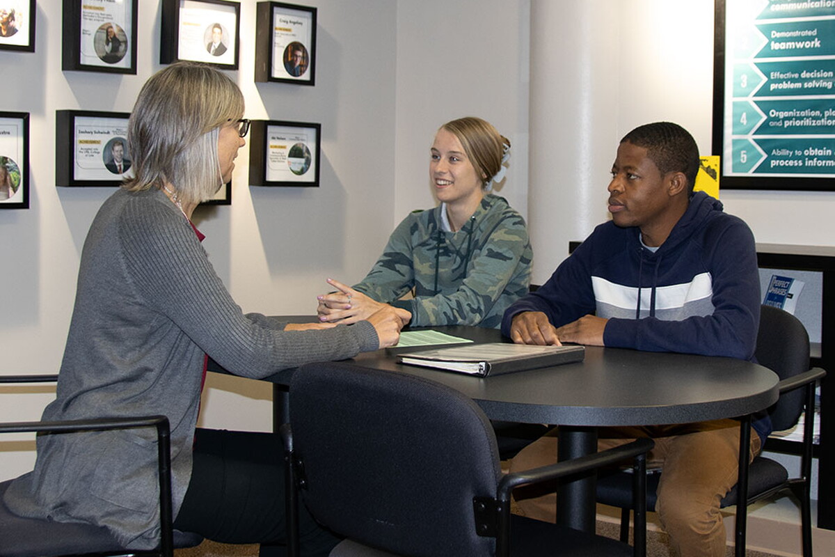 NWU administrator sits with two students at a table in a conference room.