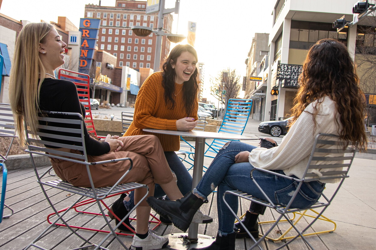 Four female NWU students sit at a table on the sidewalk of downtown Lincoln.