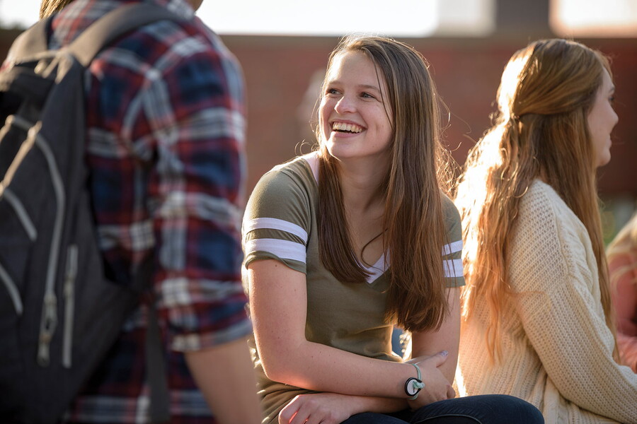 College student sitting outside smiling while talking to friends