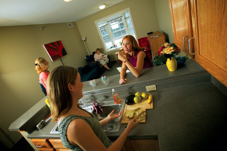 Young women hanging out in the kitchen and living room of a townhouse apartment.