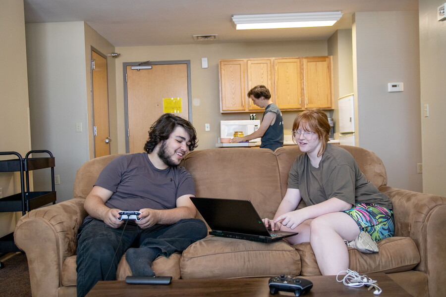 A male and female on a couch looking at a computer with a young man in the kitchen behind them.