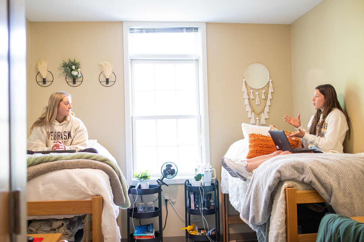 Two young women sitting across from each other on raised beds in a suite room.