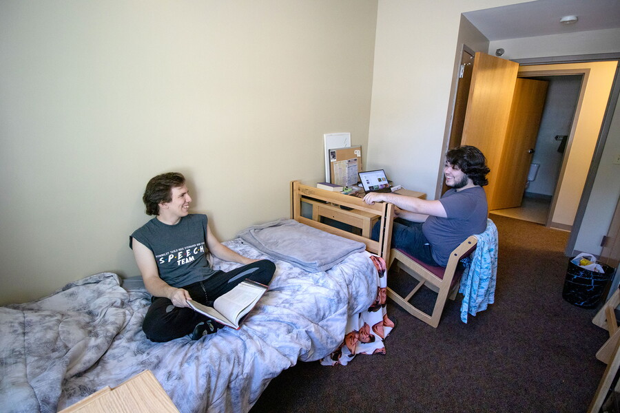 Two young men talking in a bedroom of a suite.