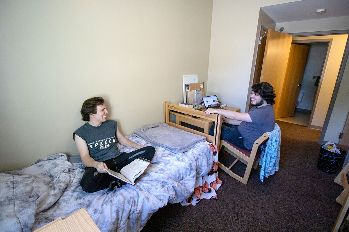 Two young men talking in a bedroom of a suite.