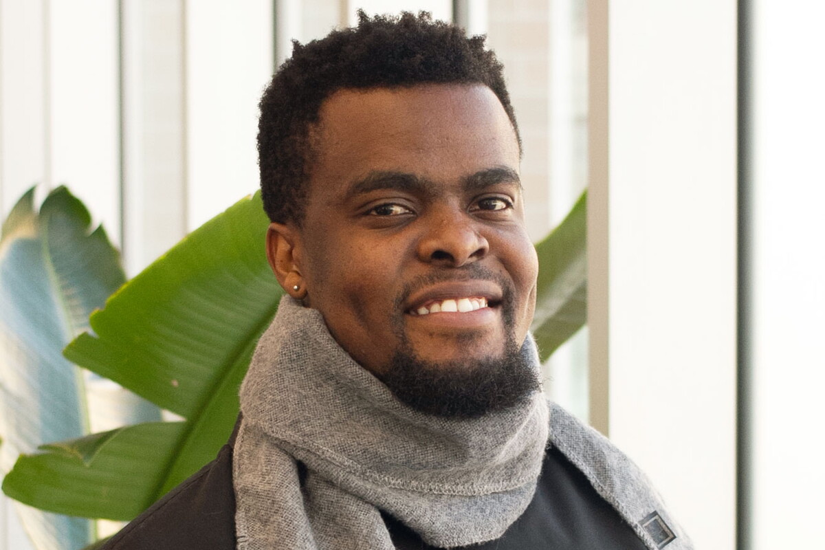 Young man with a scarf around his neck smiling.