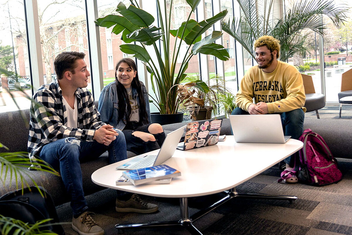 Three students study in the lobby of the Acklie building at a table.