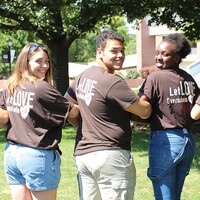 Linking arms three students turn to face the camera showing "Love Overwhelms Fear" on the back of their t-shirts.