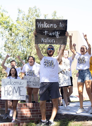 Group of NWU students cheer while holding welcome signs for students moving in.