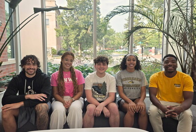 Five students sitting in a line on chairs and a couch.