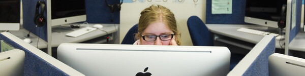 Female student in a cubical looking at a large monitor surrounded by cubicles with large monitors.